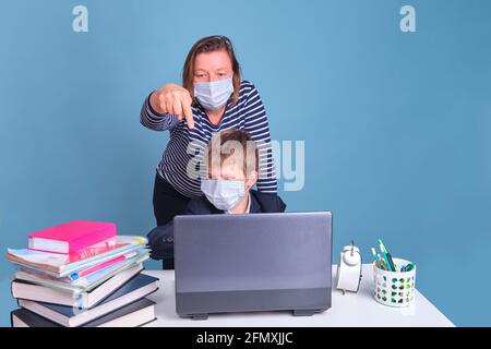 Mamma e figlio durante l'apprendimento a distanza nella scuola elementare, concetto di problemi su sfondo blu Foto Stock