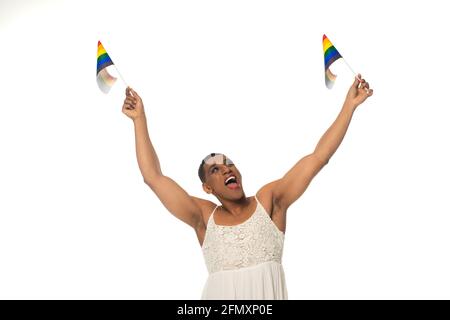 eccitato afroamericano androgino uomo in sundress tenendo lgbt bandiere in mani sollevate isolato su bianco Foto Stock