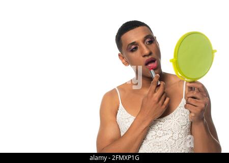 uomo transgender afroamericano in spogliatore che tiene lo specchio e che si applica rossetto isolato su bianco Foto Stock