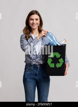 Riutilizzo della plastica. Contenitore nero Millennial Lady positivo riempito con bottiglie vuote Foto Stock