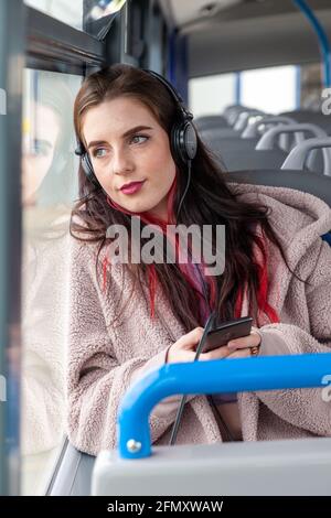 Una bella giovane donna seduta su un autobus ascoltare musica attraverso gli auricolari e guardando fuori dalla finestra Foto Stock