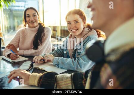 Gruppo allegro di studenti in una discussione nella scuola superiore. I giovani sorridono mentre studiano nel campus universitario. Foto Stock