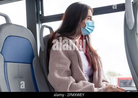 una donna che indossa una maschera facciale su un autobus e. guardando fuori dalla finestra Foto Stock