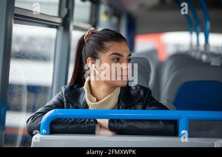 Una bella donna seduta in un autobus e che ascolta musica attraverso gli auricolari Foto Stock