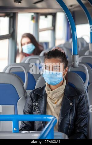 Una donna che viaggia su un autobus con una maschera facciale, con un'altra donna che si trova più indietro nell'autobus. Foto Stock