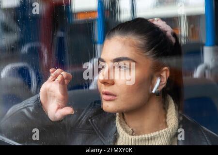Ragazza che si stende dalla finestra piovosa su un autobus Foto Stock