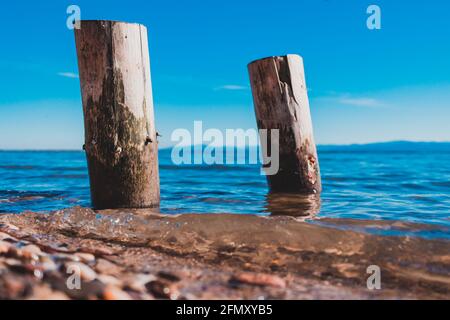 due pile di legno lavate dalle acque blu del lago con le montagne sullo sfondo Foto Stock