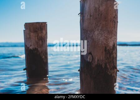 due pile di legno lavate dalle acque blu del lago con le montagne sullo sfondo Foto Stock