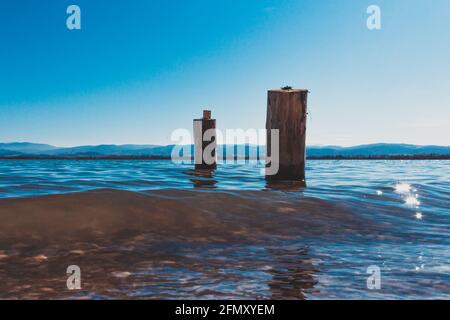 due pile di legno lavate dalle acque blu del lago con le montagne sullo sfondo Foto Stock