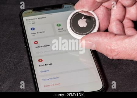 Morgantown, WV - 12 maggio 2021: Apple AirTag dispositivo tenuto in mano caustasiana senior sopra iPhone mini smartphone Foto Stock