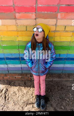 La ragazza adolescente si trova vicino a una parete arcobaleno-colorata all'esterno. Concetto di auto-amore. Stile di vita del bambino. Foto Stock