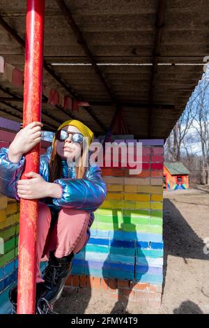 La ragazza adolescente si trova vicino a una parete arcobaleno-colorata all'esterno. Concetto di auto-amore. Stile di vita del bambino. Foto Stock