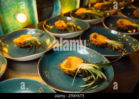 Le metà di ananas giacciono su un piatto rotondo blu, i piatti si stendono in fila. Le metà di ananas giacciono senza polpa. Foto Stock