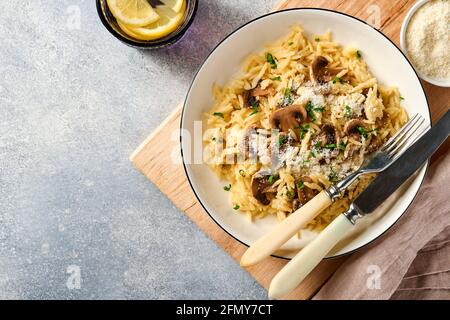 Pranzo risoni di pasta italiana, funghi, salsa, parmigiano, timo, aglio, olio d'oliva, in piastra bianca su ardesia, pietra o fondo di cemento. Vista dall'alto w Foto Stock