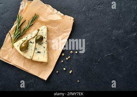 Pezzi di formaggio blu o brie su pezzetto di carta pergamena con miele, rosmarino, capperi e pepe. Messa a fuoco selettiva. Spazio libero per il testo. Foto Stock