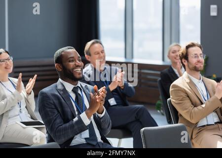 uomo d'affari afro-americano applaudendo con i partecipanti multietnici durante il seminario Foto Stock