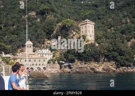 I turisti arrivano in barca a destinazione, l'abbazia di San Fruttuoso e la vicina torre Doria in una baia chiusa con una piccola spiaggia. Foto Stock