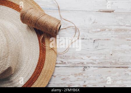 una matassa di spago beige e un cappello di paglia su uno sfondo di legno. spago per l'ago Foto Stock