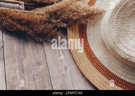 cappello marrone paglierino e beige e rami secchi di canne su sfondo ligneo. cappello estivo con brim Foto Stock