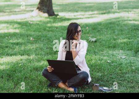 Donna d'affari che siede nel parco estivo dell'erba usando il laptop. Un uomo d'affari lavora a distanza durante la messa a fuoco selettiva di Quarantine.Soft. Foto Stock