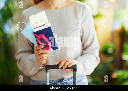 Viaggio durante la pandemia del coronavirus. Primo piano su donna di 40 anni con un agente antibatterico, borsa carrello, biglietti aerei, maschera medica e covid passpo Foto Stock