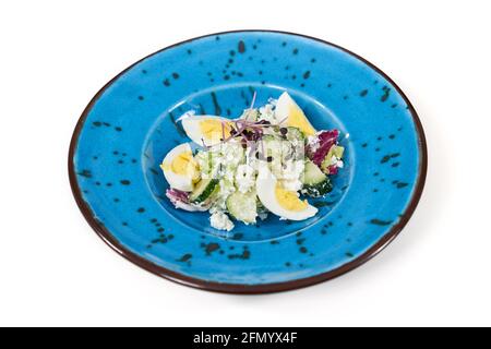 Primo piano di un bel piatto blu moderno con deliziosa insalata con verdure e uova su sfondo bianco. Concetto di insalata appetitosa con vitamine sane per l'emaciazione. Foto Stock