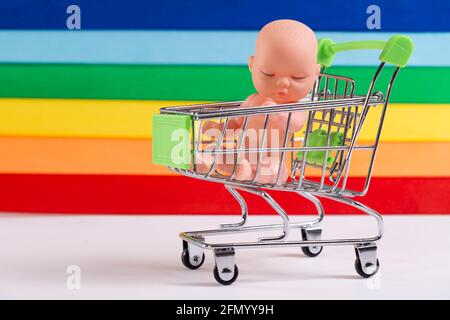 Comunità LGBT e bambini. Baby doll in un cestino della spesa sullo sfondo della bandiera LGBT, il concetto di adozione, inseminazione artificiale. Foto Stock