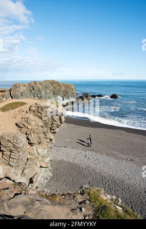 La gente cammina sulla spiaggia di sabbia nera, lungo le scogliere e le formazioni rocciose a Fauskasandur, nell'Islanda orientale. Foto Stock