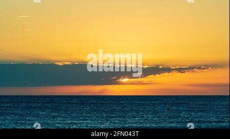 L'epico e colorato tramonto illumina le nuvole di rosso e arancione su blu acque Foto Stock