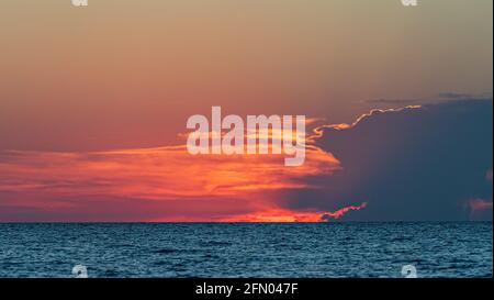 L'epico e colorato tramonto illumina le nuvole di rosso e arancione su blu acque Foto Stock