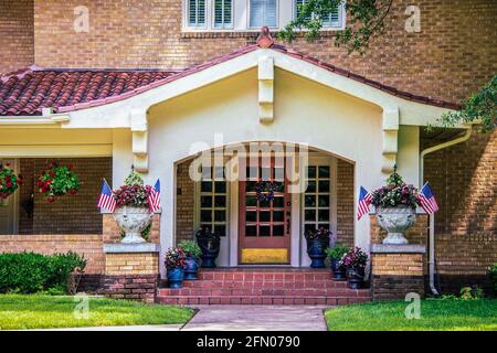 Ingresso e stuco bungalow portico con porte e piastrelle francesi Tetto su casa di mattoni con molti vasi di fiori e americano bandiere e corona di porte a forma di stella Foto Stock