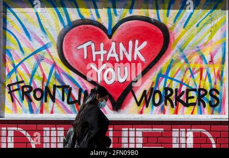 Toronto, Canada. 12 maggio 2021. Una donna che indossa una maschera facciale cammina oltre un murale a Toronto, Ontario, Canada, il 12 maggio 2021. A partire da mercoledì pomeriggio, il Canada ha riportato un totale complessivo di 1,305,174 casi COVID-19, di cui 24,765 morti, secondo CTV. Credit: Zou Zheng/Xinhua/Alamy Live News Foto Stock