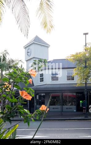 Kerikeri, Nuova Zelanda, Nuova Zelanda - 12 maggio 2021: Torre dell'Orologio e negozi al dettaglio nella strada principale con fiori di ibisco e fronde di palme Foto Stock