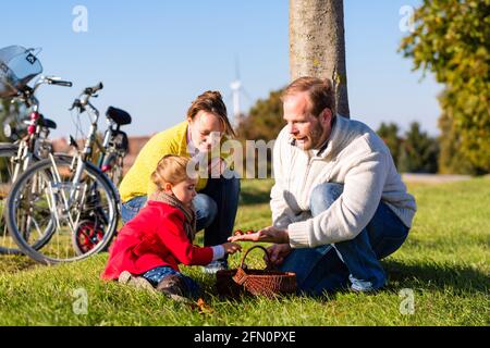 Famiglia con madre, padre e figlia di viaggio con la famiglia in bicicletta o ciclo di lavoro in posizione di parcheggio o paese la raccolta delle castagne Foto Stock