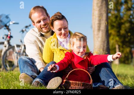 Famiglia con madre, padre e figlia di viaggio con la famiglia in bicicletta o ciclo di lavoro in posizione di parcheggio o paese la raccolta delle castagne Foto Stock