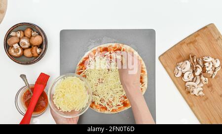 Le mani della donna condiscono l'impasto della pizza con mozzarella, vista ravvicinata dall'alto. Passo dopo passo ricetta fatta in casa per la pizza con mozzarella e funghi Foto Stock