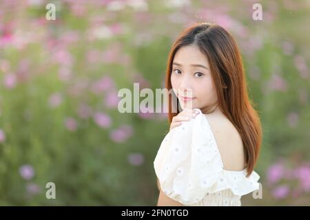 Bella giovane donna con abito bianco su fiori di cosmo rosa sfondo Foto Stock