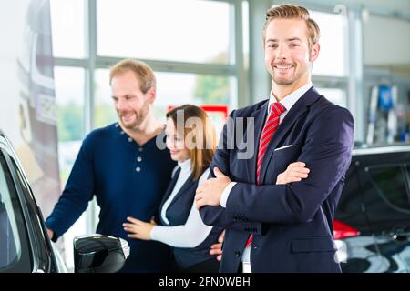 Venditore o venditore auto e i clienti o i clienti in concessionaria auto presentando la decorazione di interni di autoveicoli nuovi e usati nello showroom Foto Stock