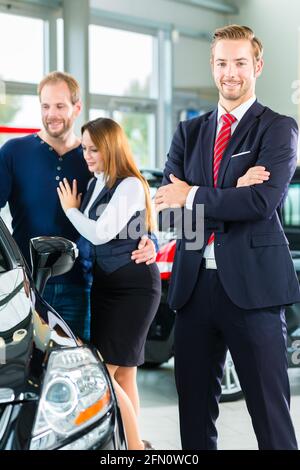 Venditore o venditore auto e i clienti o i clienti in concessionaria auto presentando la decorazione di interni di autoveicoli nuovi e usati nello showroom Foto Stock