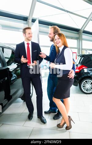 Venditore o venditore auto e i clienti o i clienti in concessionaria auto presentando la decorazione di interni di autoveicoli nuovi e usati nello showroom Foto Stock