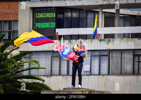 Passo, Colombia. 12 maggio 2021. Demostrator ondeggia la bandiera della Colombia nel luogo dove si trovava la statua di Antonio Narino, che fu rimossa la notte prima con una recinzione dietro di lui che dice: 'Costruire progressi' nel centro della città di Pato, Narino il 12 maggio 2021 credito: Long Visual Press/Alamy Live News Foto Stock