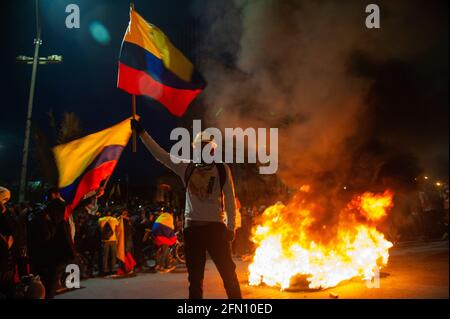 Bogota, Cundinamarca, Colombia. 12 maggio 2021. Un dimostratore fa ondere una bandiera colombiana davanti a un pit-Fire di pneumatici come Bogotà, la Colombia entra la sua terza settimana di proteste antigovernative contro il presidente Ivan Duque Marquez e le morti che si sommano fino a 40 in casi di brutalità della polizia durante lo Sciopero Nazionale, il 12 maggio 2021. Credit: Chepa Beltran/LongVisual/ZUMA Wire/Alamy Live News Foto Stock