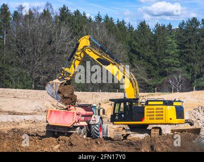 Falda terra gialla che riempie un autocarro in un cantiere Foto Stock