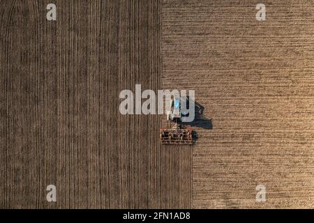Vista dall'alto di un trattore che erala terreno in un campo agricolo. Dissodamento o preparazione di terreno. Foto Stock