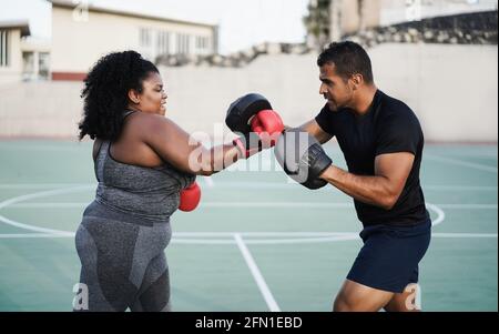 Donna curvy e personal trainer che fa sessione di allenamento di boxe all'aperto - fuoco principale sul fronte dell'allenatore Foto Stock