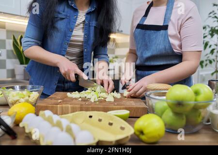 Primo piano di mano di madre e ragazza affettando verde mele sul tagliere della cucina Foto Stock