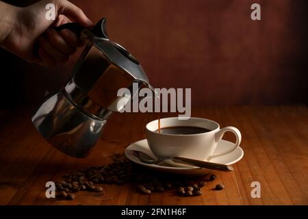 Vista ravvicinata della mano femminile che versa il caffè dal caffè pentola in tazza su tavolo di legno Foto Stock