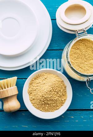 Utilizzo di polvere di senape per il lavaggio del concetto di piatti. Piastre bianche pulite con recipiente di polvere di senape gialla e vaso con spazzola per lavare i piatti in legno. Foto Stock