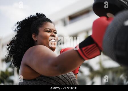 Donna curvy e personal trainer che fa sessione di allenamento di boxe all'aperto - mettere a fuoco sul viso Foto Stock