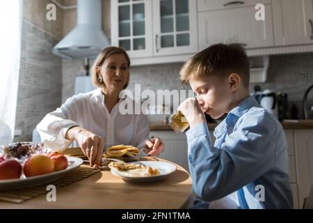 Donna adulta in cucina tratta un bambino con frittelle e succo di frutta. Foto Stock